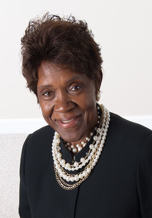A woman wearing a black jacket and pearls smiles for the camera