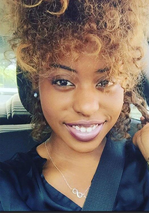 A woman with curly hair is wearing an infinity necklace