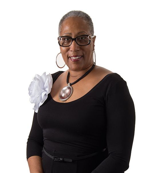 A woman wearing glasses and a black top has a flower on her shoulder