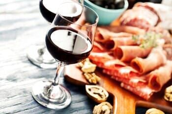A cutting board with meat , nuts , and wine glasses on it.