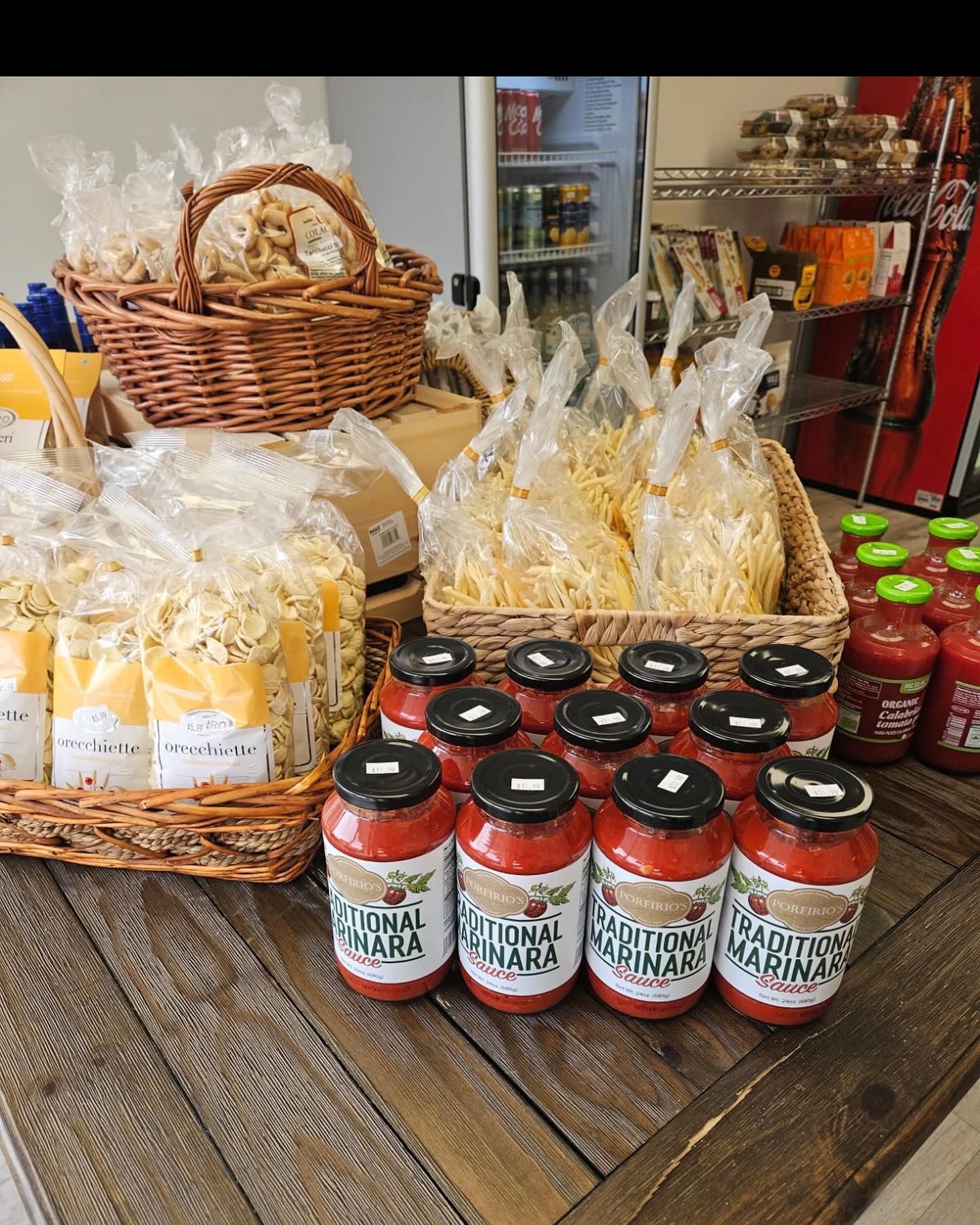 A wooden table topped with jars of tomato sauce and a basket of pasta.