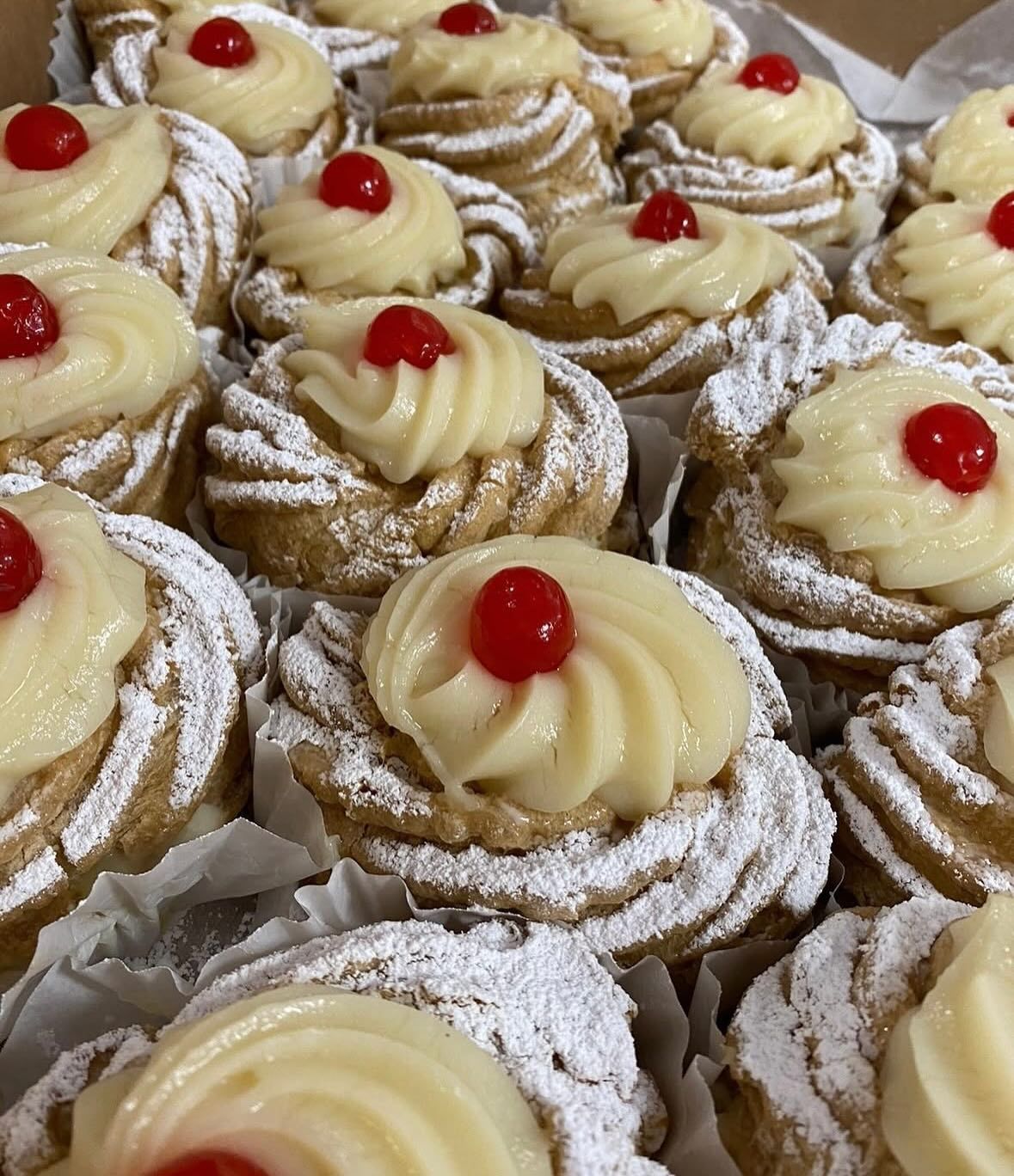 A box of cupcakes with frosting and cherries on top