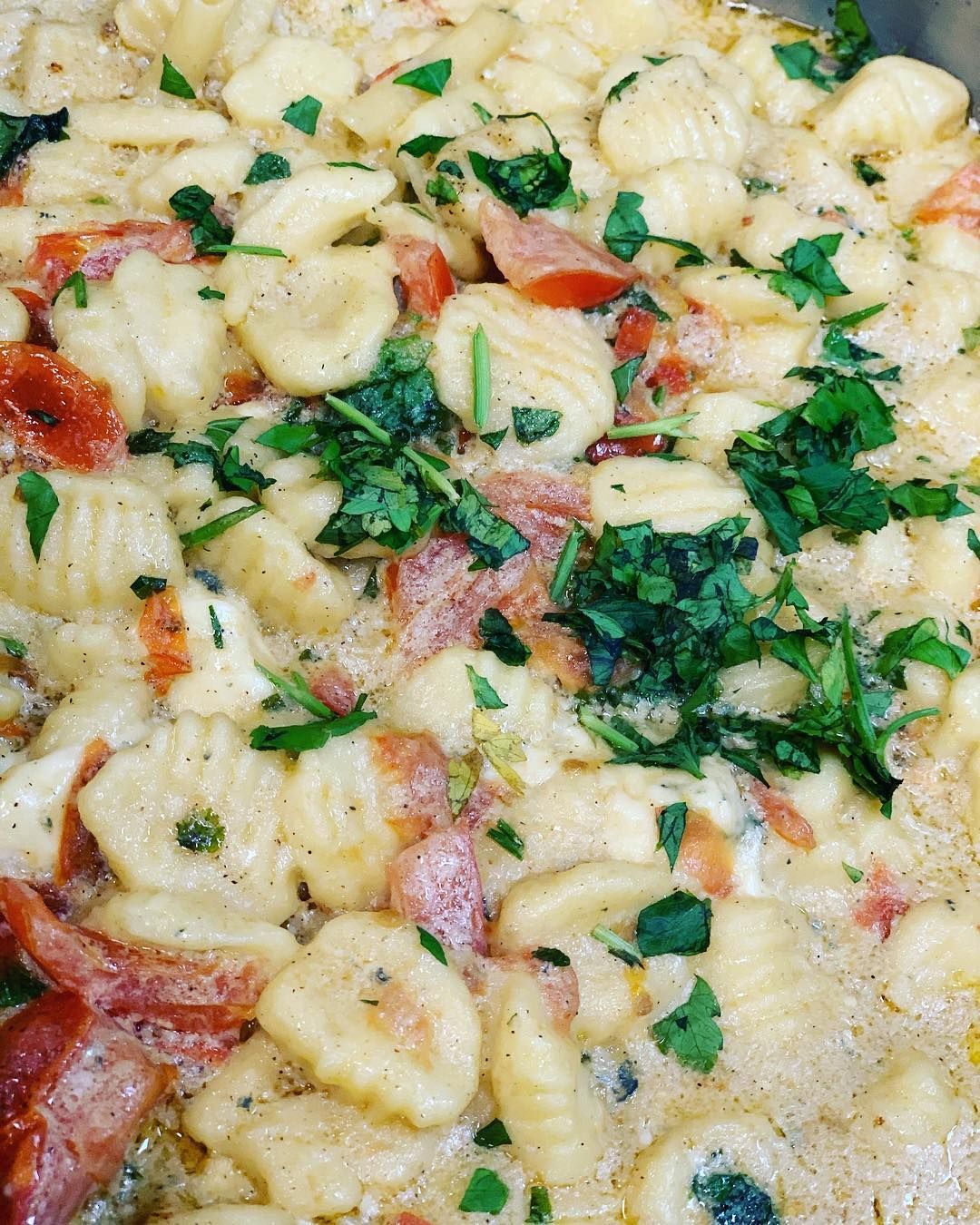 A close up of a casserole dish filled with pasta , tomatoes and parsley.