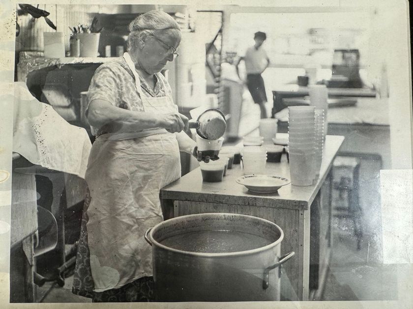 A black and white photo of an elderly woman cooking in a kitchen