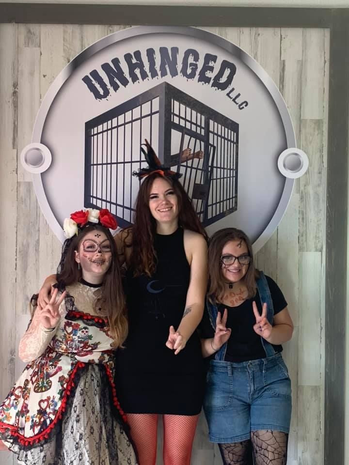 Three women are posing for a picture in front of a sign that says unchanged llc.