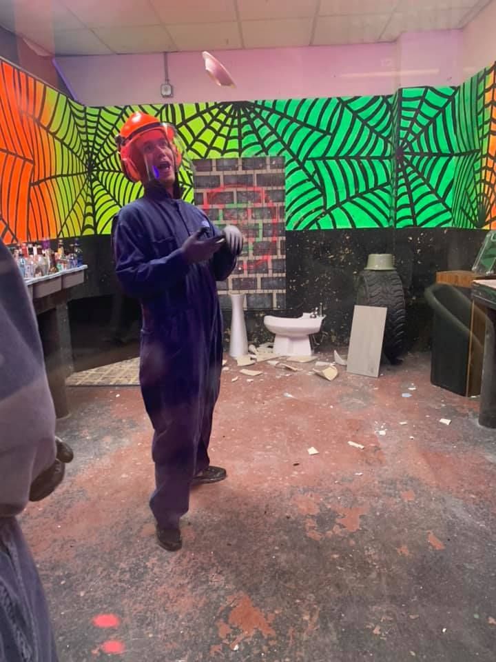 A man in a purple jumpsuit is standing in a room with a toilet.