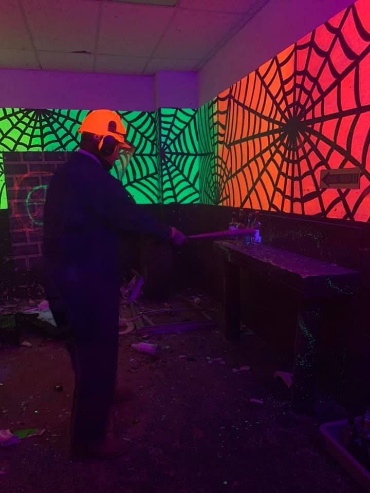 A man is standing in a room with neon spider webs painted on the walls.