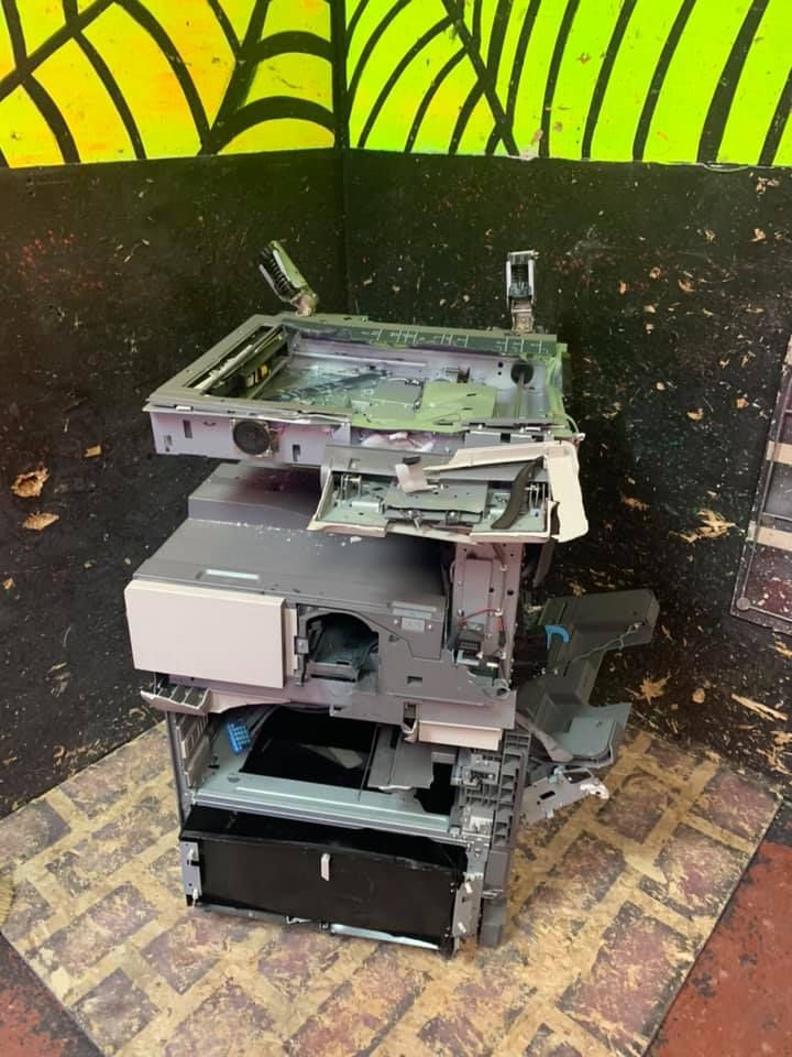 A broken printer is sitting on top of a brick floor.