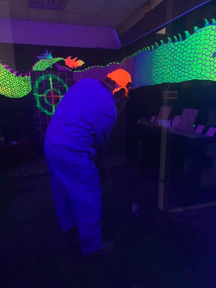 A person is standing in front of a glow in the dark dragon.