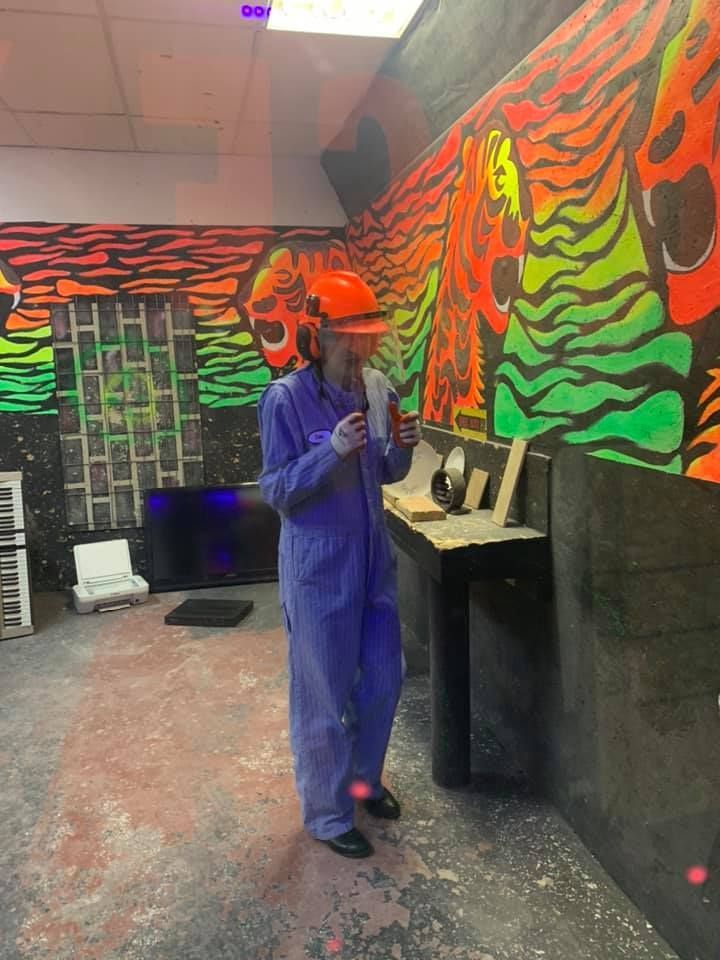 A person in a blue jumpsuit is standing in a room with a mural on the wall.