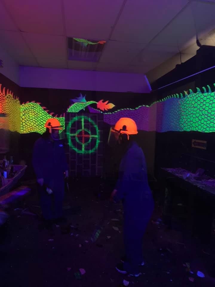 A group of people are standing in a dark room with neon lights on the walls.
