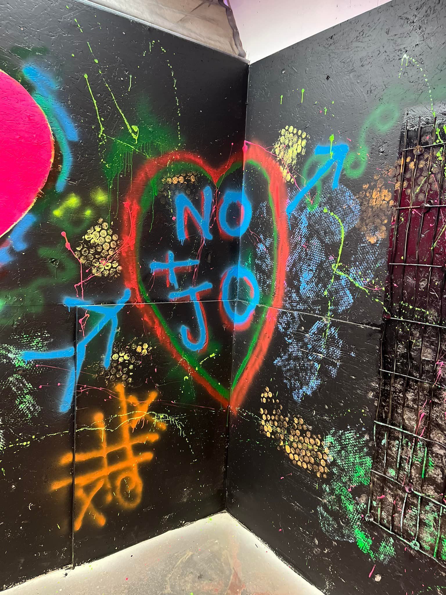 A corner of a room with graffiti on the wall including a heart and the words `` no jo ''.