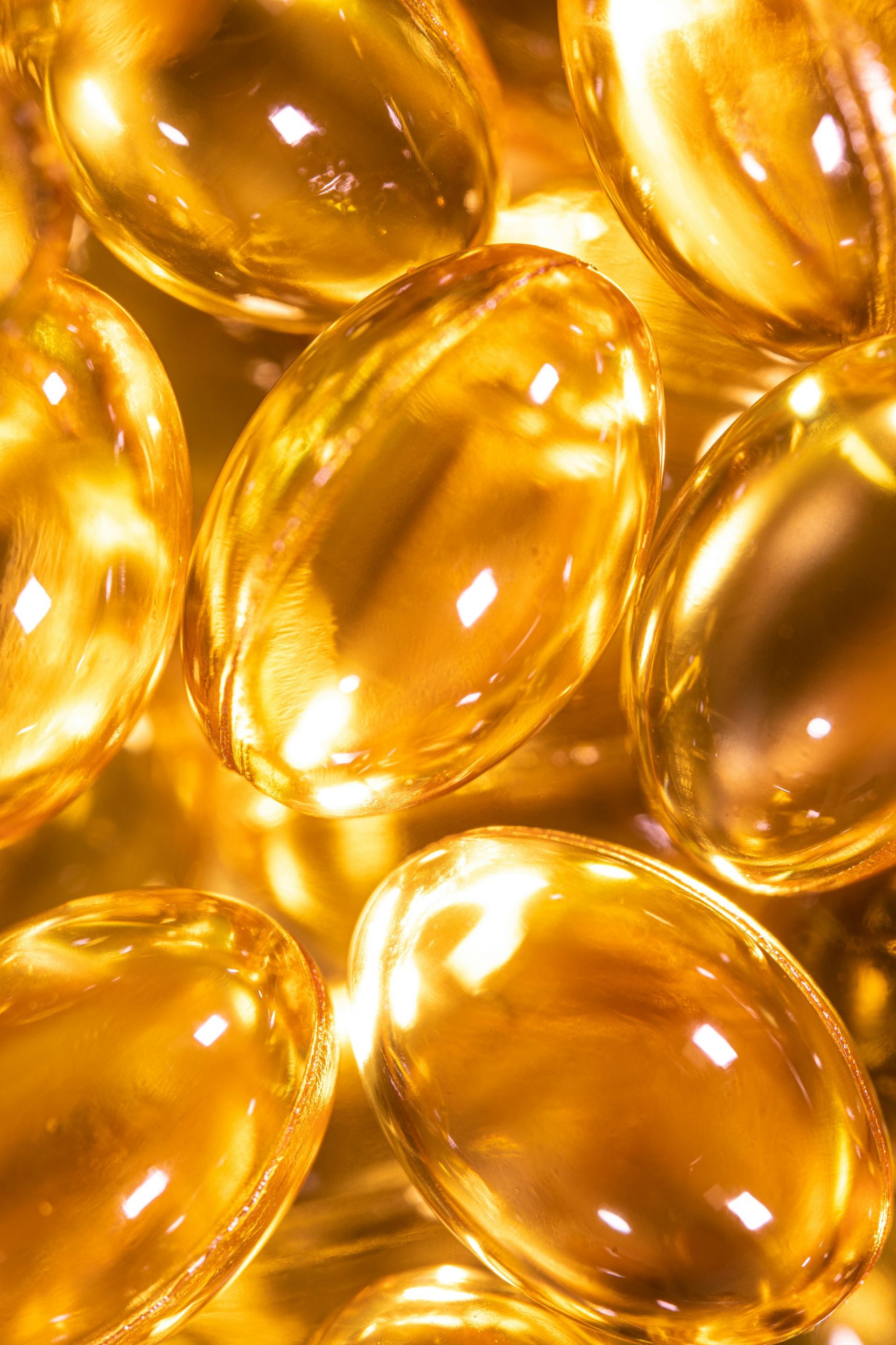 A close-up view of multiple translucent, golden, oval-shaped softgel vitamin capsules stacked together.