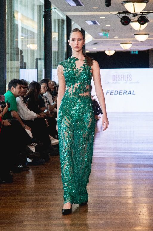 Una mujer camina por una pasarela con un vestido blanco y dorado.