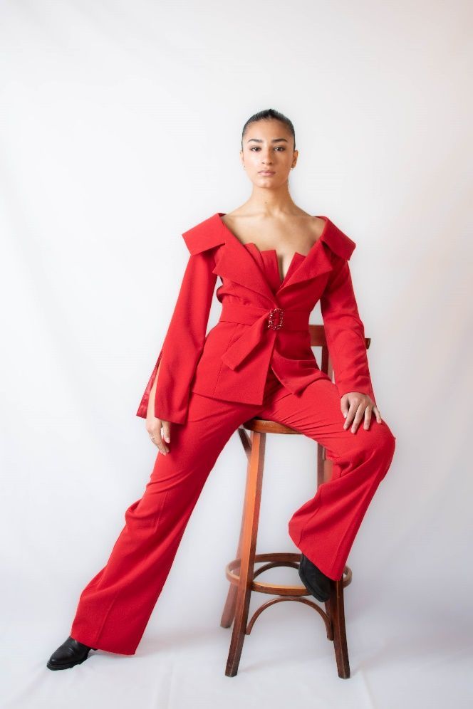 Una mujer con un traje rojo está sentada en un taburete.