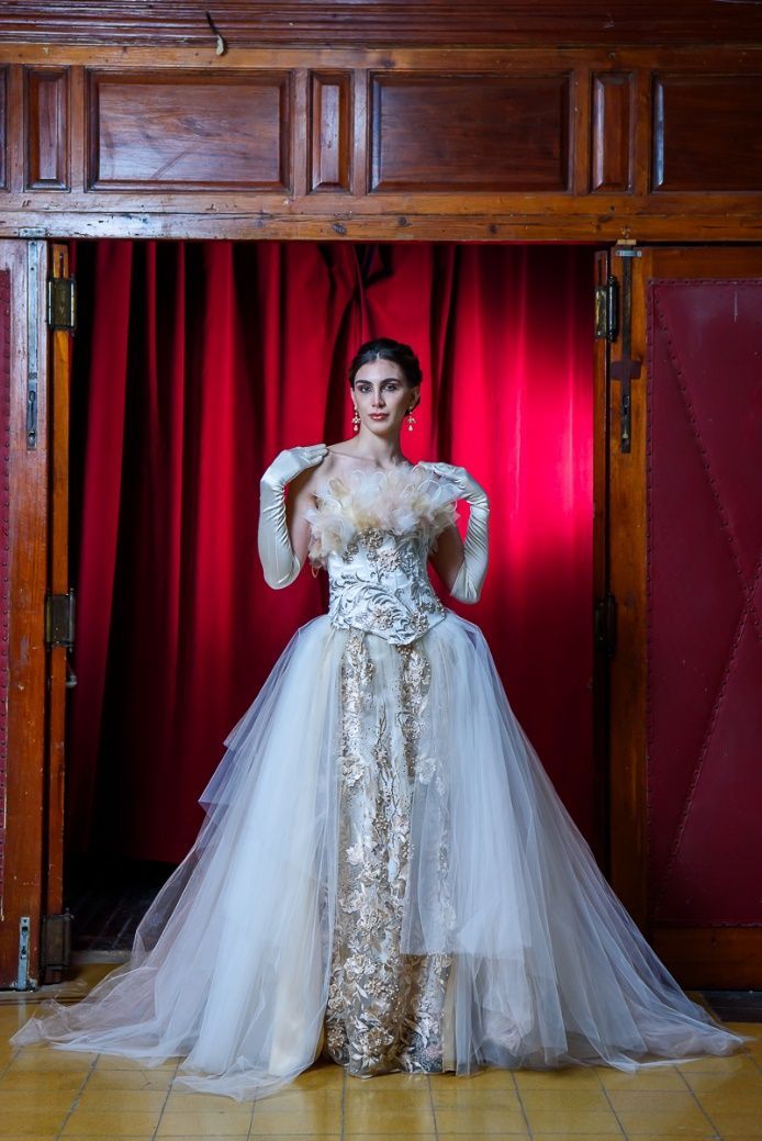 Una mujer con un vestido blanco está parada frente a una cortina roja.
