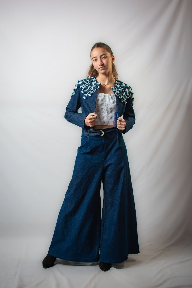 Una mujer lleva una chaqueta azul y pantalones anchos.