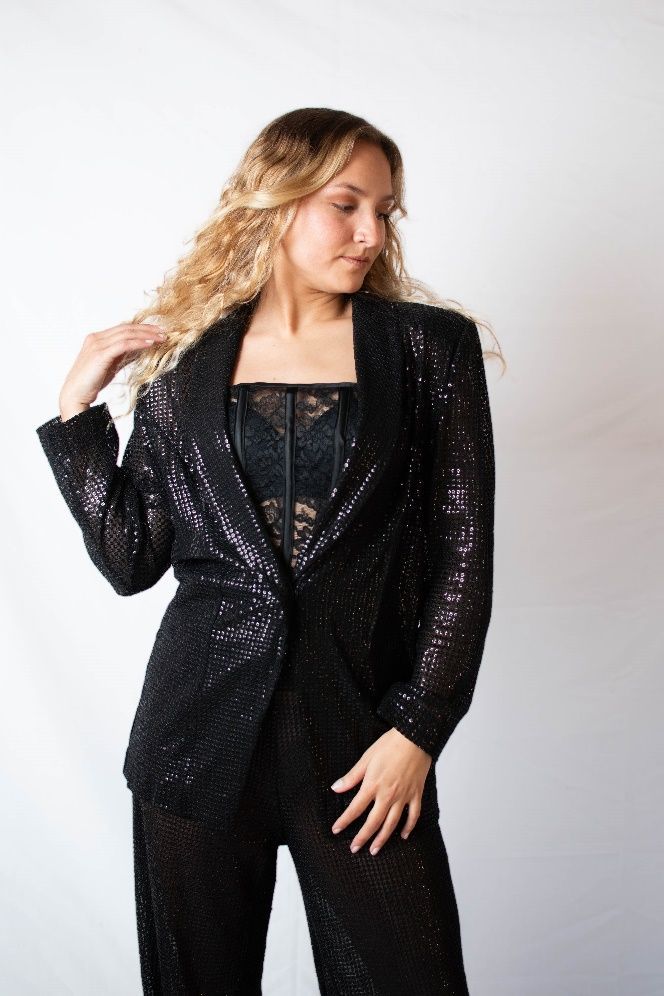 Una mujer con un corsé de encaje negro y pantalones está parada frente a una pared blanca.