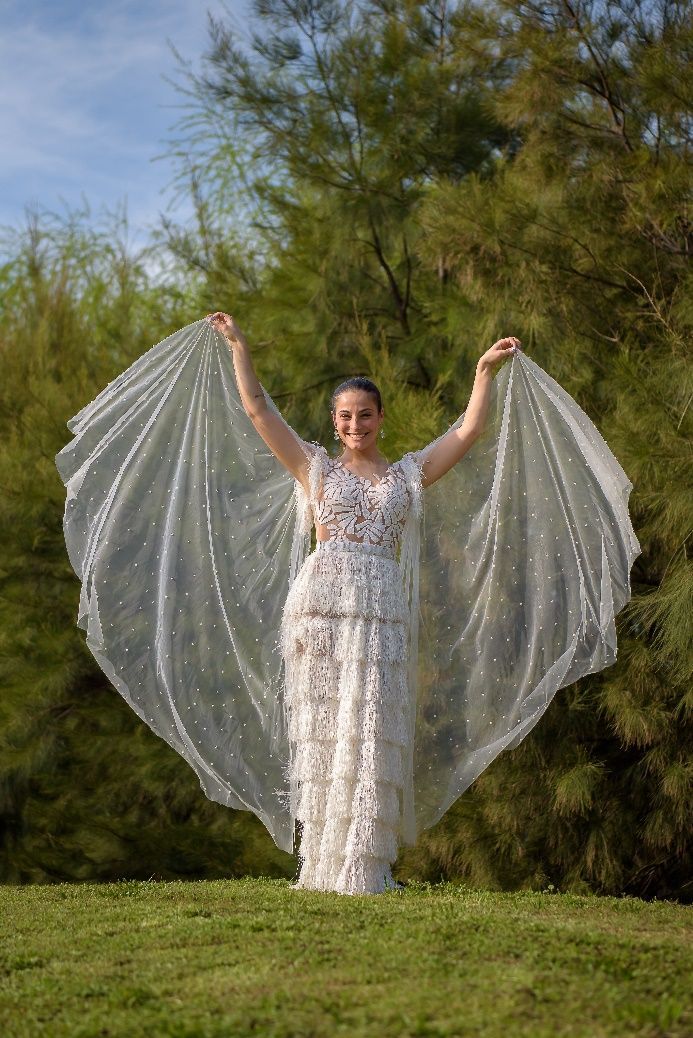 Una mujer con un vestido blanco está parada en un campo con los brazos extendidos.