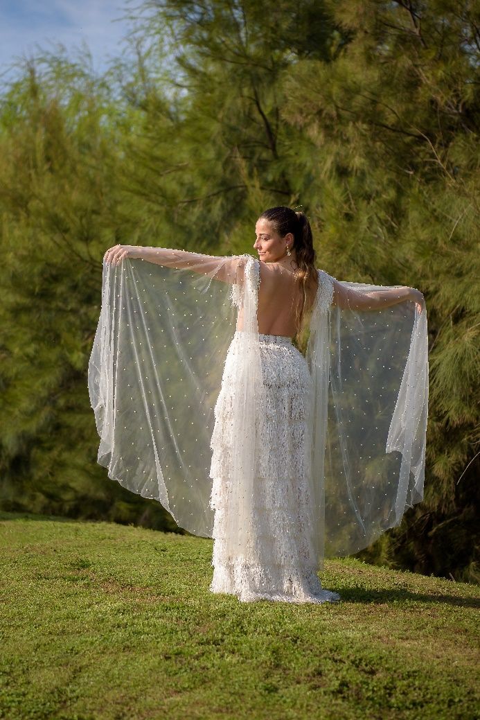Una mujer con un vestido blanco está parada en un campo con los brazos extendidos.