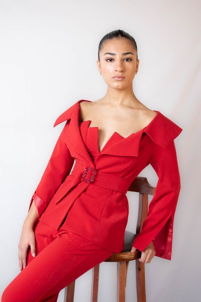 Una mujer con un traje rojo está sentada en un taburete.