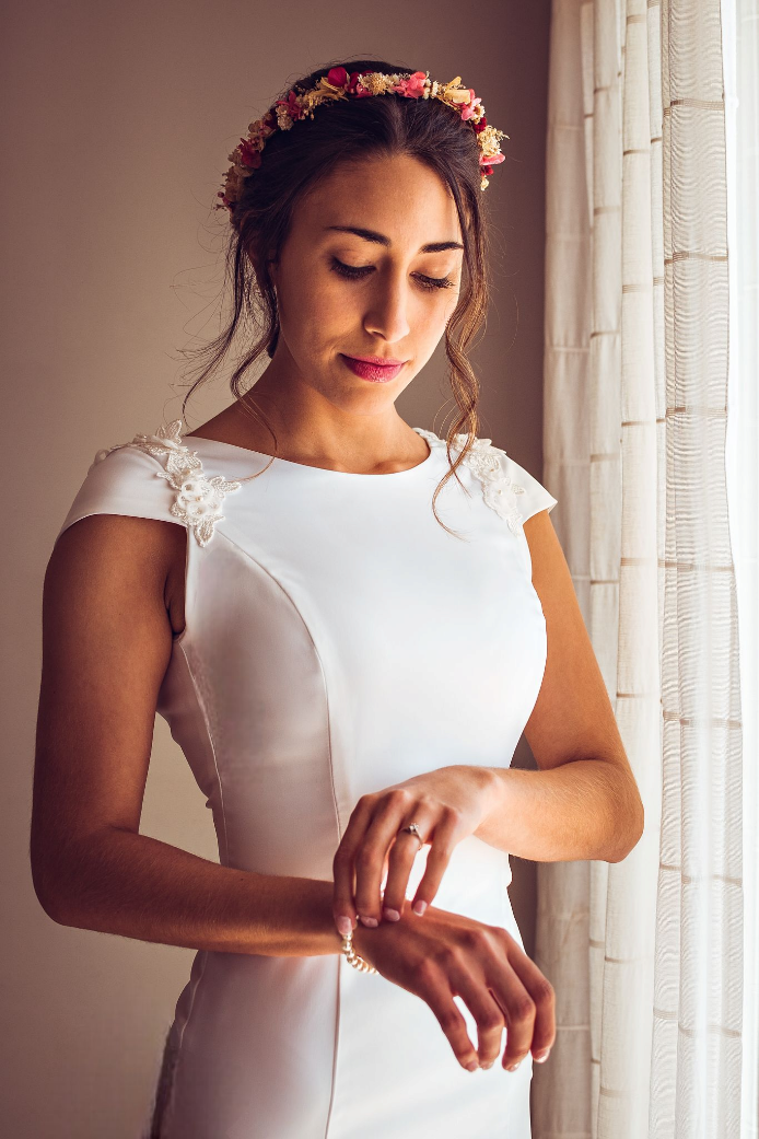 Una mujer con un vestido de novia está parada frente a un sofá sosteniendo un ramo de flores.