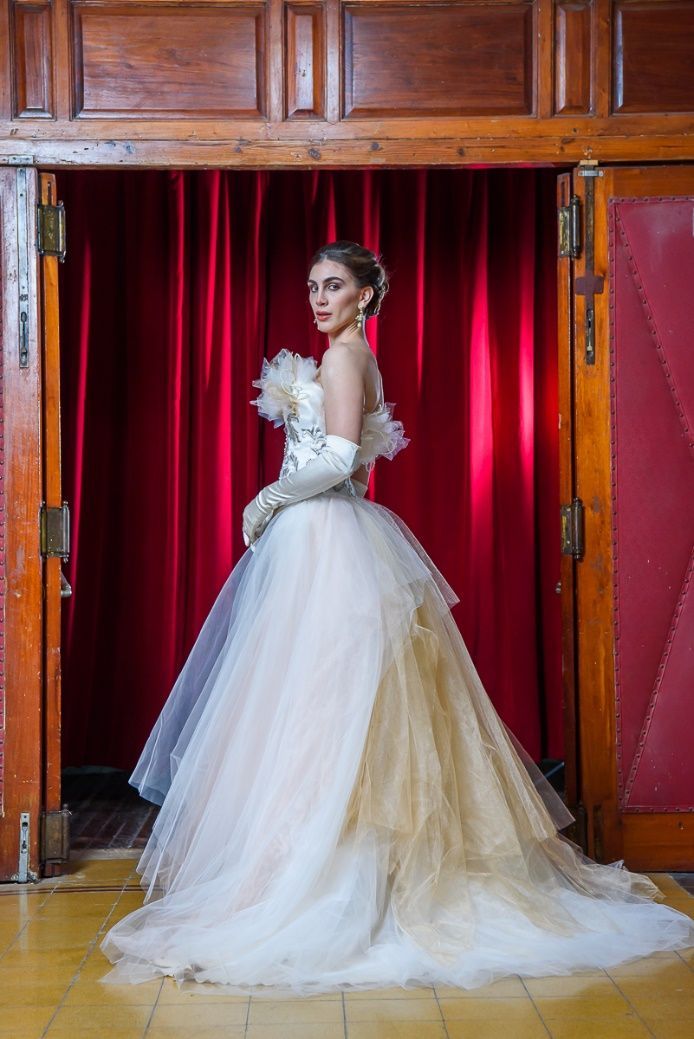 Una mujer con un vestido blanco está parada frente a una cortina roja.