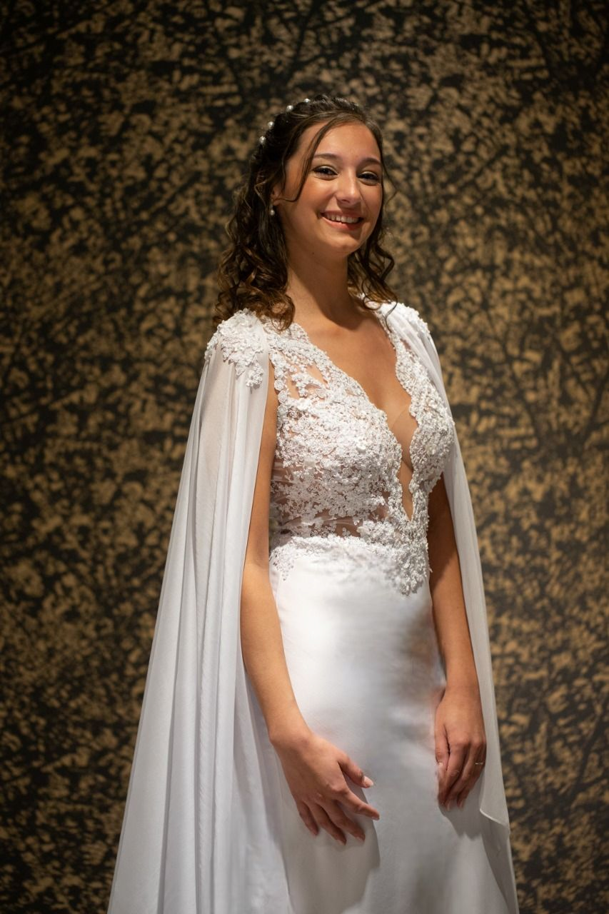 Una mujer con un vestido de novia blanco y una capa está parada frente a una pared.