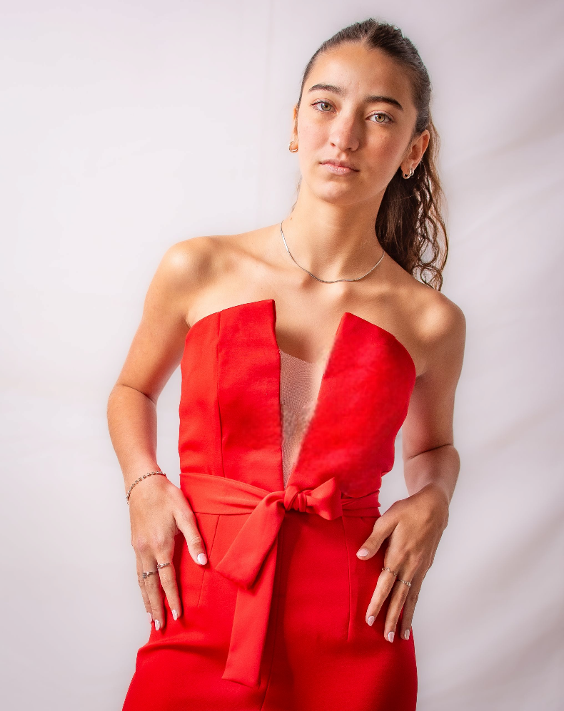 Una mujer con un vestido rojo está parada frente a una pared blanca.