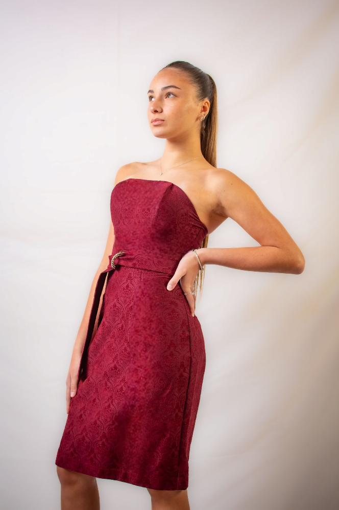 Una mujer con un vestido rojo sin tirantes está parada frente a una pared blanca.