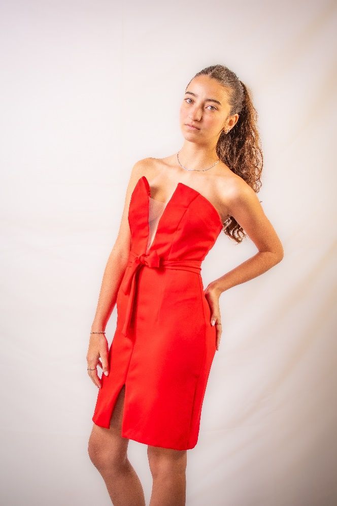 Una mujer con un vestido rojo está parada frente a una pared blanca.