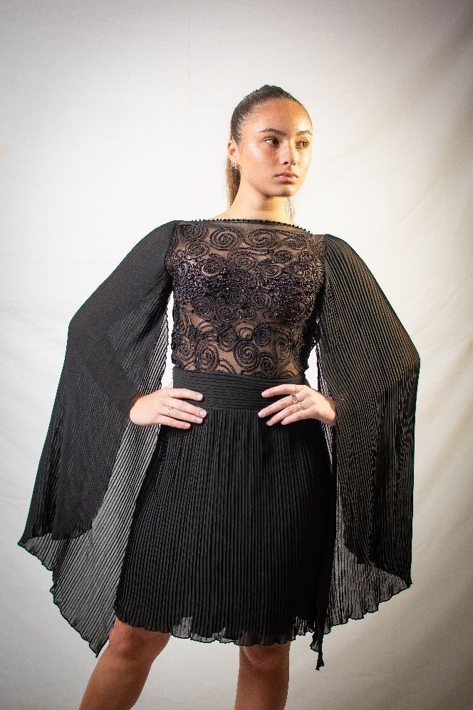 Una mujer lleva un vestido negro con una capa en las mangas.