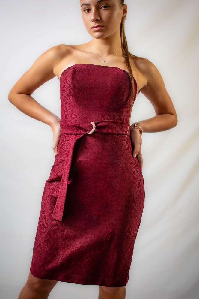 Una mujer con un vestido rojo sin tirantes está parada frente a una pared blanca.