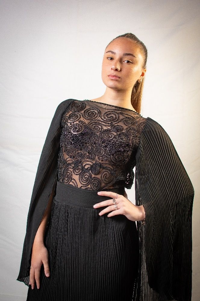 Una mujer lleva un vestido negro con una capa en las mangas.