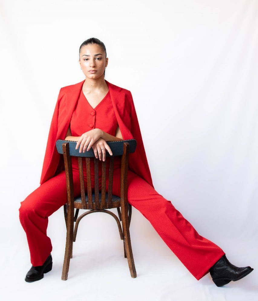 Una mujer con un traje rojo está parada frente a una pared blanca.