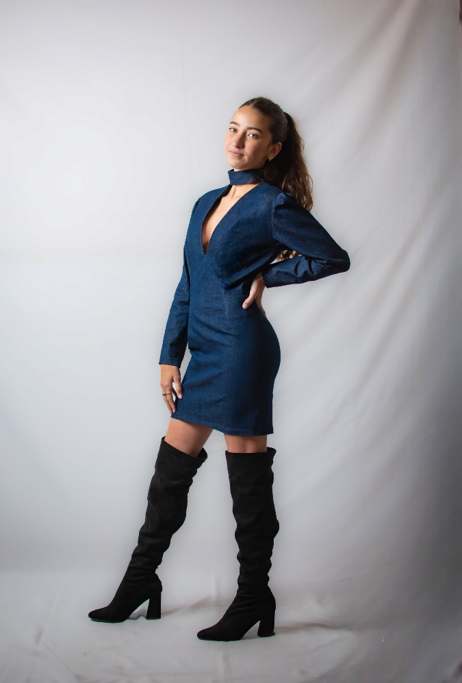 Una mujer con un vestido azul y botas negras está de pie sobre un fondo blanco.