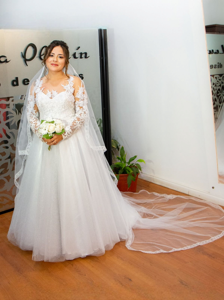 Una mujer con un vestido de novia está parada frente a un espejo sosteniendo un ramo de flores.