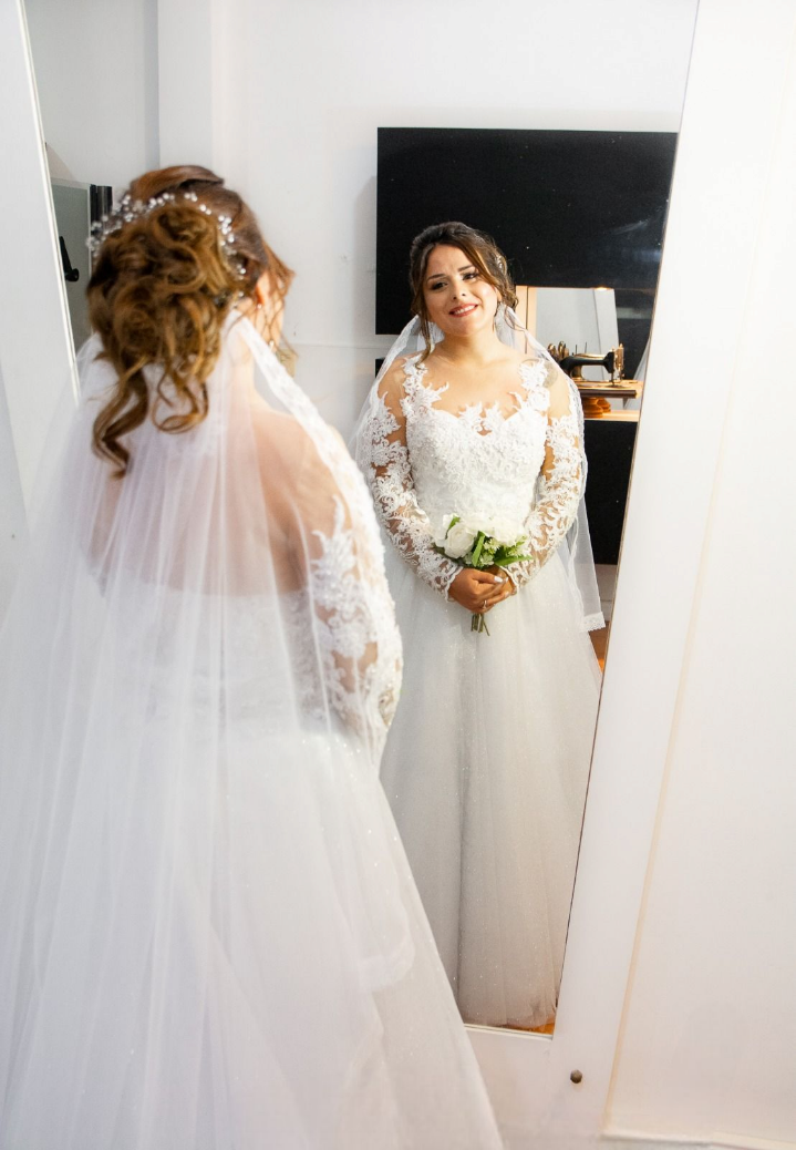 Una mujer con un vestido de novia está parada frente a un espejo sosteniendo un ramo de flores.
