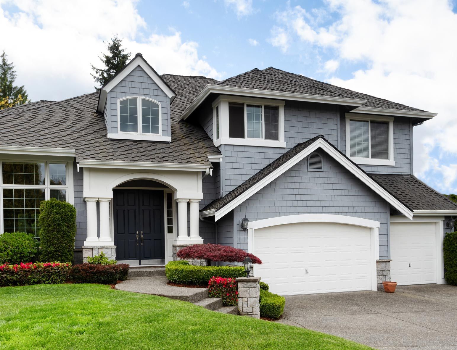 A large gray and white house with a gray roof and white garage doors.