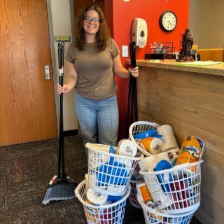 Woman holding broom, supplies near a counter, ready to clean.
