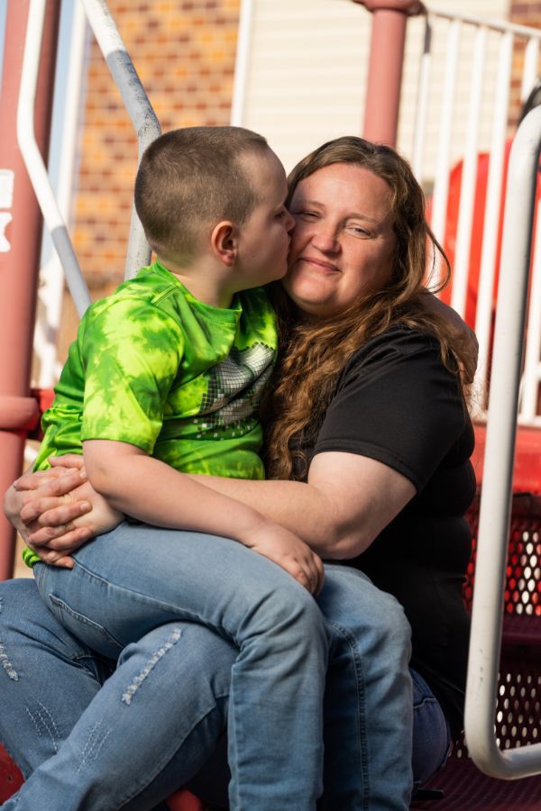 A child kisses a smiling woman on the cheek; they are on a playground.