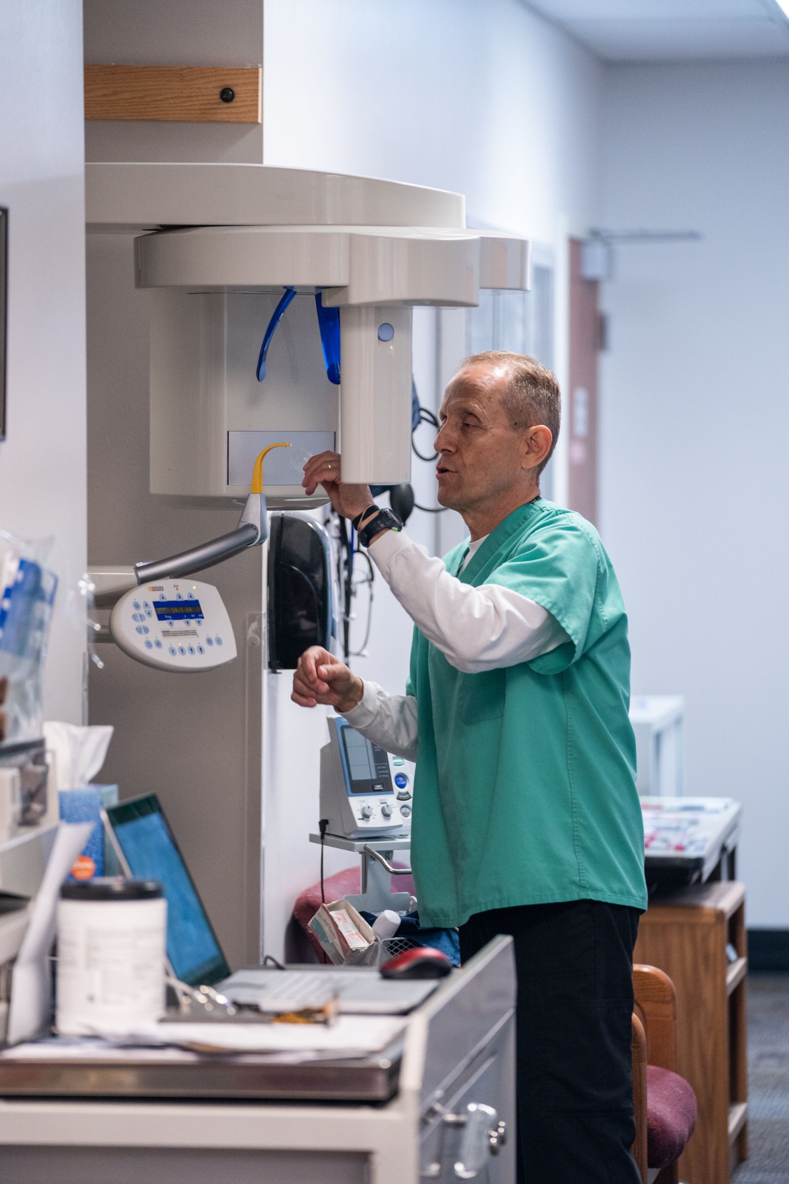 Dentist in green scrubs adjusts dental X-ray machine in a clinic.