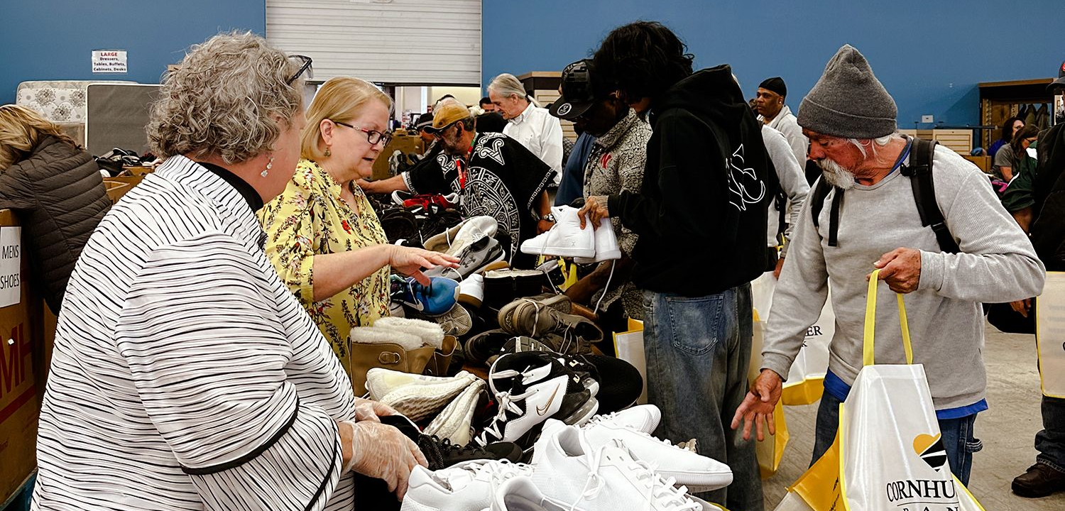 People at a shoe giveaway event. Volunteers give shoes to people; setting inside a large room.