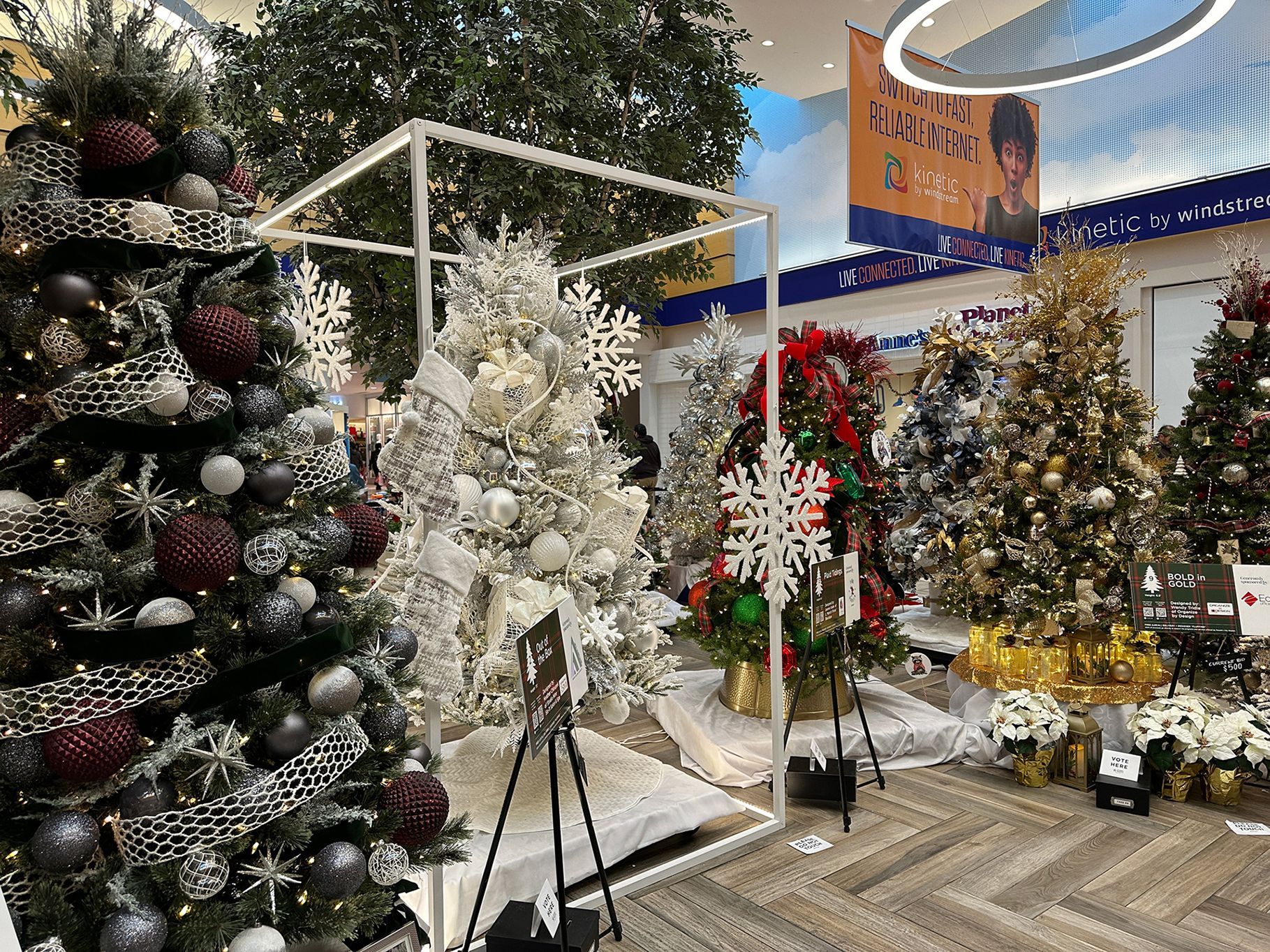 Christmas trees decorated with ornaments and ribbons, on display in a mall setting.