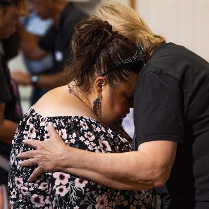 Woman being embraced, head bowed in prayer; another woman's hands on her back.