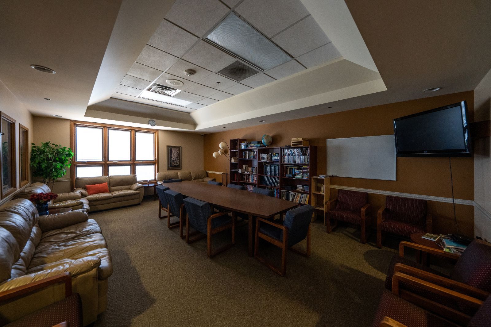 A meeting room with a large table, sofas, chairs, bookshelves, and a TV.
