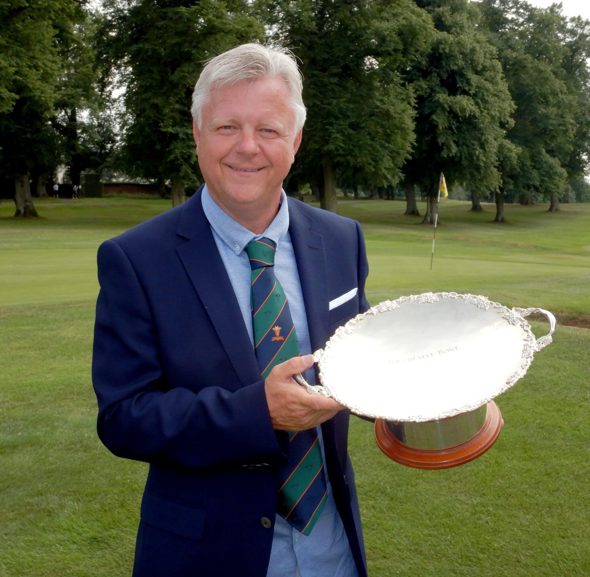 John Rawlings in a suit and tie is holding a trophy