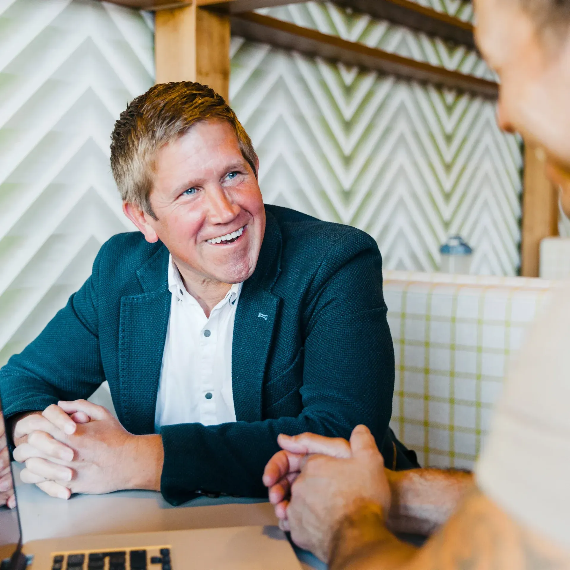 Ben Cooper in a suit is smiling while sitting at a table with another man.