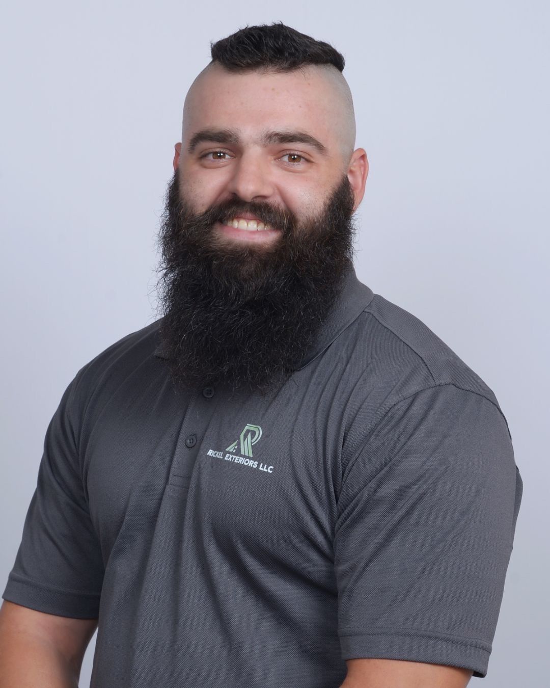 Man with shaved head and large beard wearing a gray polo shirt, smiling.