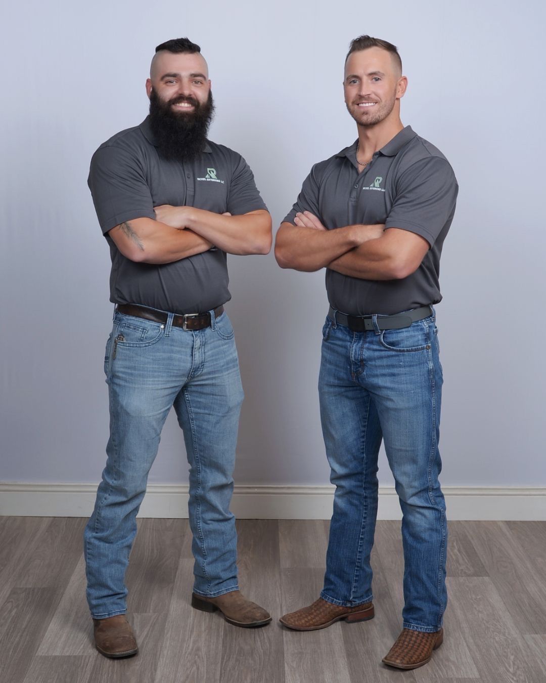 Two men with arms crossed, in gray polo shirts and blue jeans, standing in a studio.